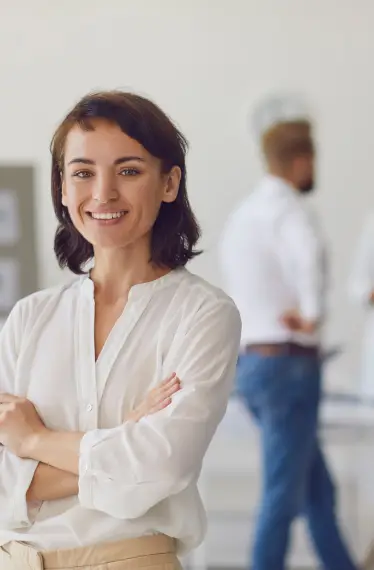 Smiling professional woman standing confidently in a modern office, representing employee satisfaction and financial wellness.